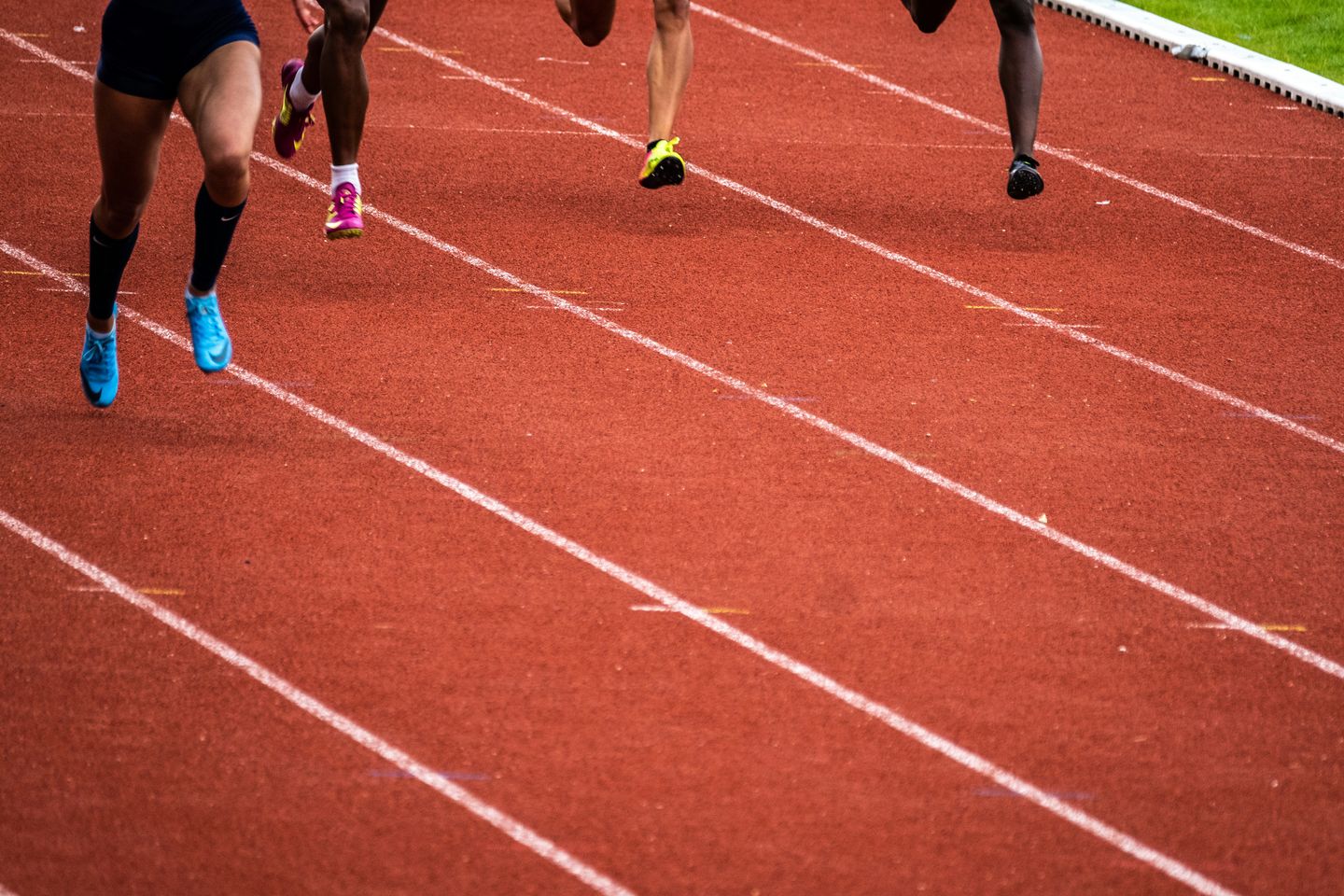 Close-up of four sprinters' legs and spiked running shoes mid-stride on a red athletics track